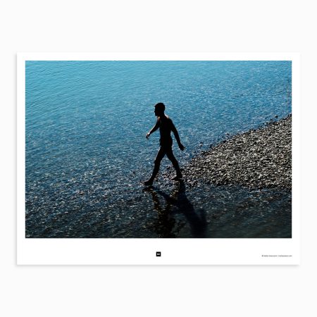 A young man casually strolls along the river bank, feeling the fine gravel under his feet while enjoying the warm summer sun. Crna Bara, Serbia, 2021.